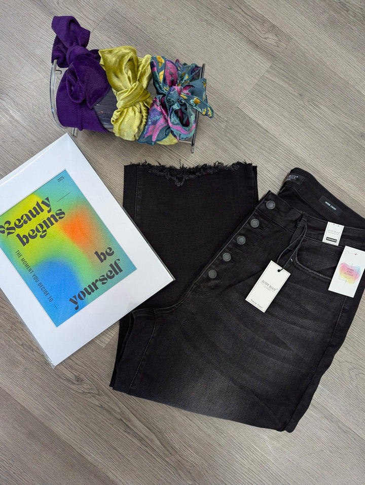 flat lay of judy blue jeans in black wash with button fly distressed hem with headbands and art print