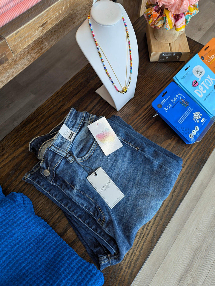 straigh leg judy blue jeans folded on table with necklace and tops around it