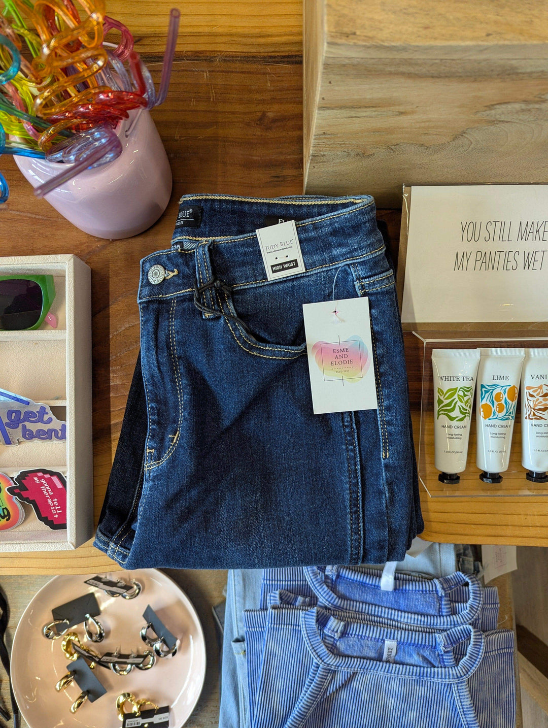 womens dark wash flared judy blue jeans folded on table with hand lotion, stickers and tank tops